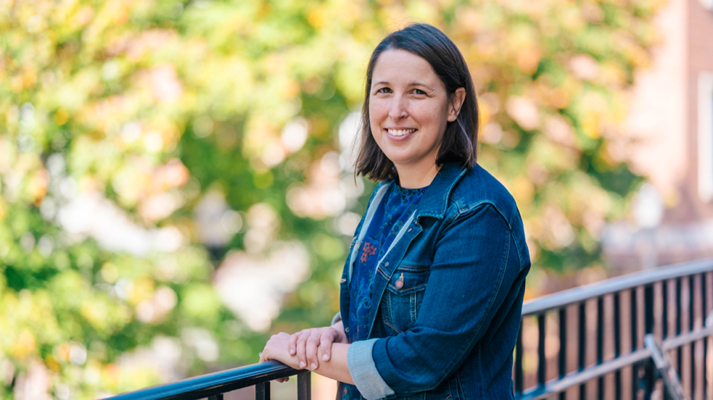 UNCG's Erin Reifsteck wears a jean jacket and leans on a metal balcony facing the camera